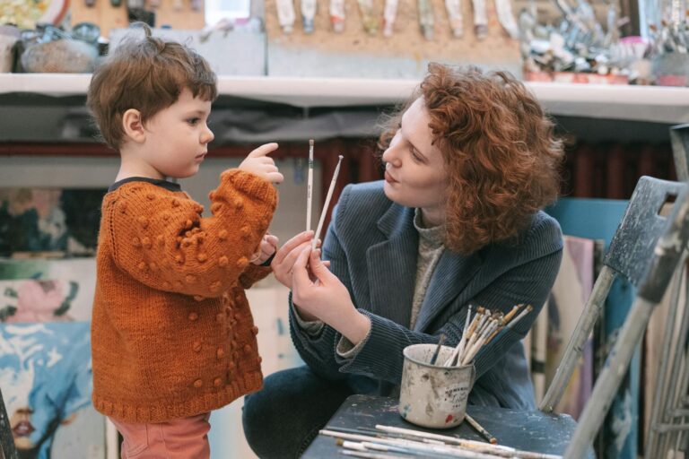 A mother and her young child painting together in a cozy art studio setting.